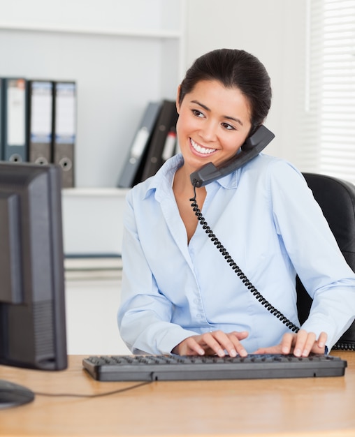 Foto affascinante donna al telefono mentre si digita su una tastiera