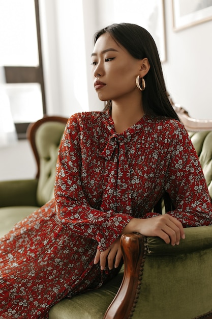 Charming woman in red floral dress sits on classic velvet green sofa