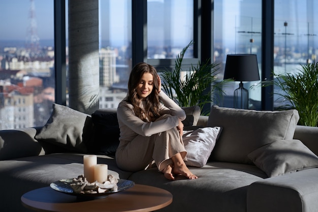 Charming woman sitting on comfy couch and enjoying sunbeams