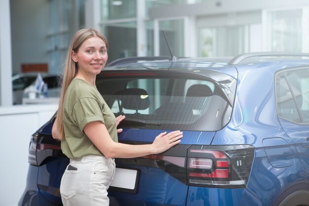 自動車販売店で新車を購入した後、カメラを喜んで笑っている魅力的な女性