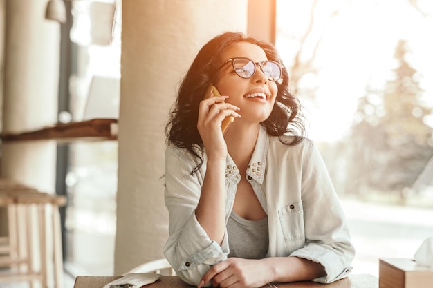 Charming woman speaking on smartphone and dreamily looking\
away