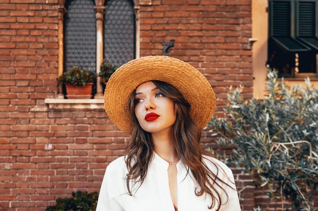 Charming woman in white blouse and straw hat. Portrait of make up girl with long hair and big red lips. Make up kit, summer vibe, concept of pure perfect skin. Beauty vacation concept