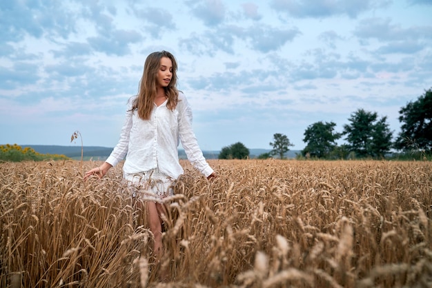 Charming woman in white dress walking on wheat field