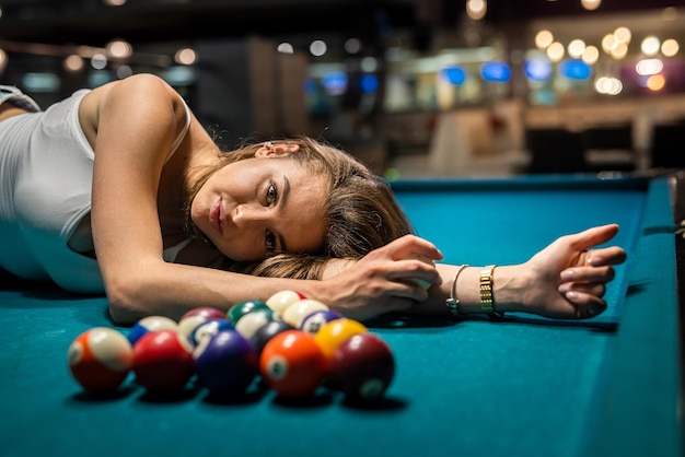 Charming woman in a white Tshirt lies on a pool table