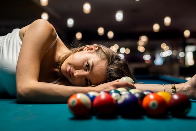 Charming woman in a white Tshirt lies on a pool table