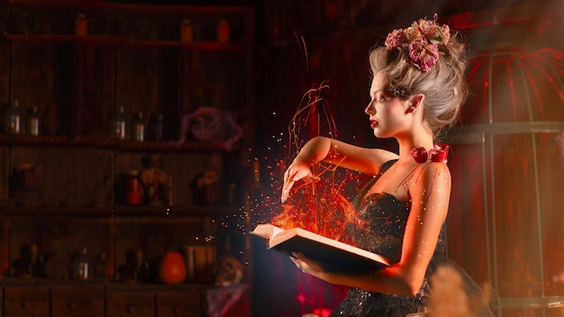 古い城の呪文の本と髪のヴィンテージの黒いドレスで魅力的な女性の魔女の花。ハロウィーン。お祝い。魔術のコンセプト、おとぎ話の神秘的な雰囲気。魔法の呪文を想起させる