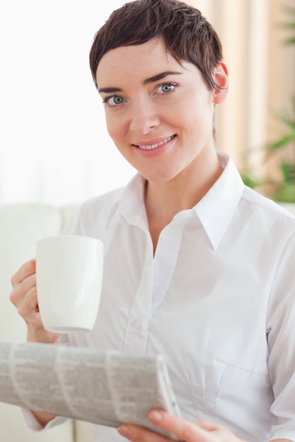 カップと新聞を持った魅力的な女性