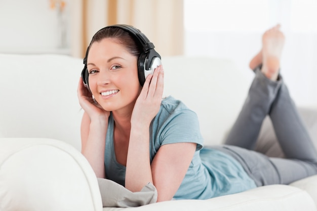 Charming woman with headphones posing while lying on a sofa