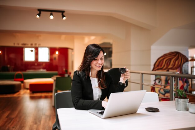 Charming woman with headphones using laptop and enjoying a cup of coffee.