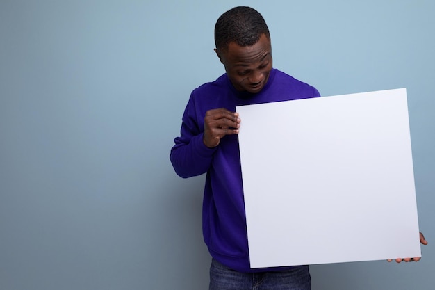 charming young african guy in a blue sweatshirt shows a promotional offer on a poster