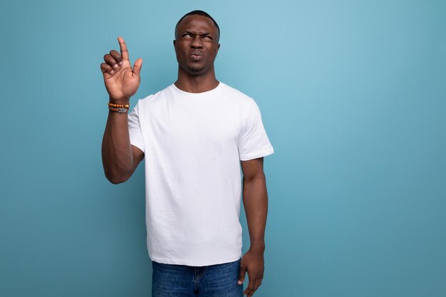 Charming young african man in white tshirt raised his hand thoughtfully on studio background with