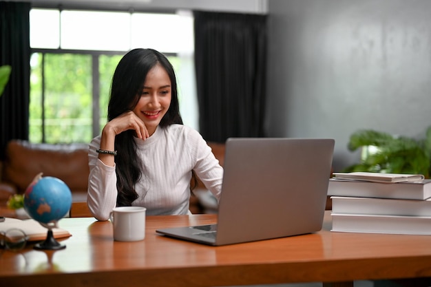 랩톱 컴퓨터를 사용하여 사무실에서 일하는 매력적인 젊은 아시아 여성