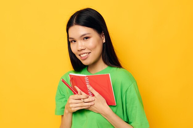 赤いノートとペンで隔離された背景が変更されていない魅力的な若いアジアの女性の緑のTシャツ高品質の写真