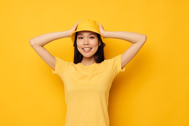 黄色い帽子をかぶった魅力的な若いアジアの女性は、感情をポーズします黄色の背景は変更されていません