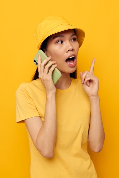 Charming young Asian woman in a yellow hat and Tshirt talking on the phone studio model unaltered