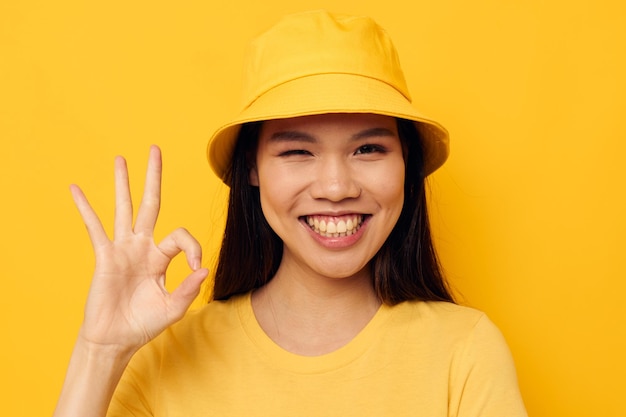 Affascinante giovane donna asiatica con una maglietta gialla e un cappello che posano emozioni stile di vita inalterato