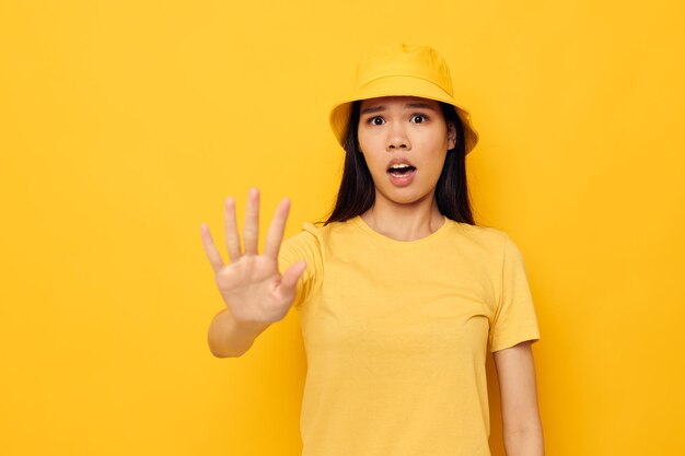 Charming young Asian woman in a yellow tshirt and hat posing emotions yellow background unaltered