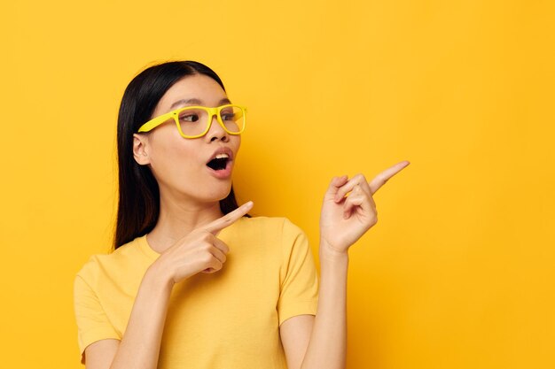 Affascinante giovane donna asiatica in magliette gialle con occhiali in posa su sfondo giallo moda inalterato