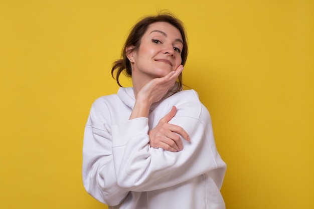 Charming young caucasian woman closing eyes in enjoyment, hugging herself, feeling comfortable and cozy, embracing herself