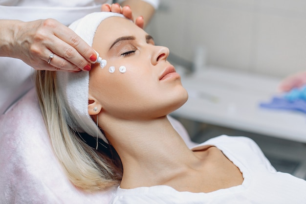 Charming young client enjoying the application of the cream to her face after a beauty treatment.