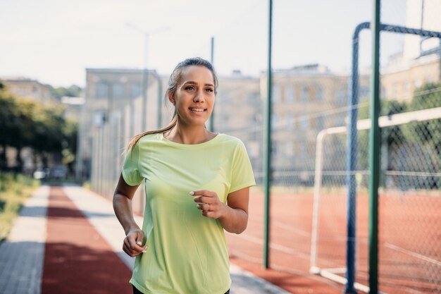 Charming young female in sport clothing jogging on treadmill at stadium.