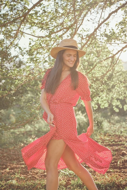 Charming young female in stylish dress and hat on grass in park on sunny day