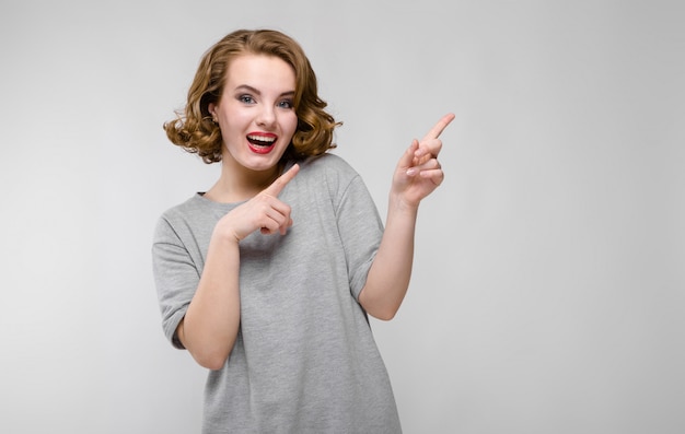 Charming young girl in a gray T-shirt on a gray background. The girl points fingers upward