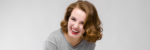 Charming young girl in a gray T-shirt on a gray background. The girl points with her finger and laughs