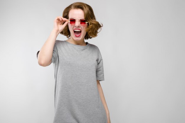 Charming young girl in a gray t-shirt on a gray background. girl in red square-eyed glasses