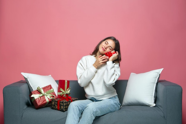 Affascinante ragazza che tiene regalo in un bel pacchetto seduto sul divano per celebrare il natale o