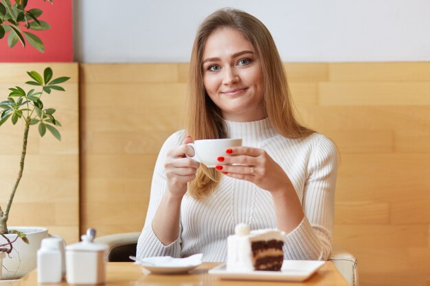 魅力的な若い女の子が熱いお茶を飲むカフェでウォームアップ