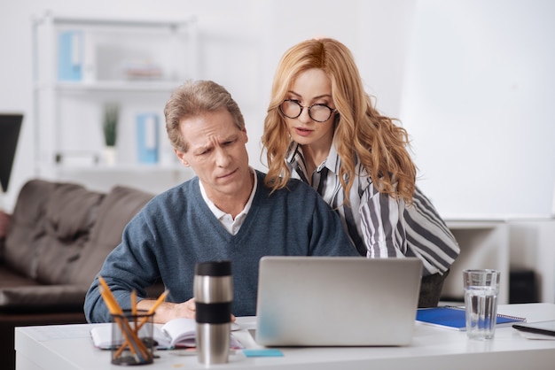 Charming young involved businesswoman standing in the office while using gadget and seducing colleague