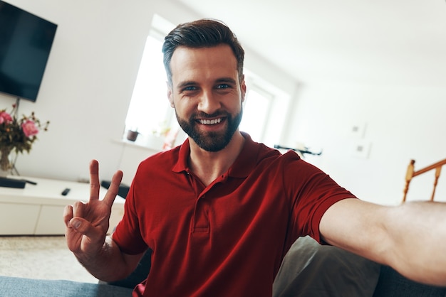 Photo charming young man in casual clothing looking at camera and smiling while spending time indoors