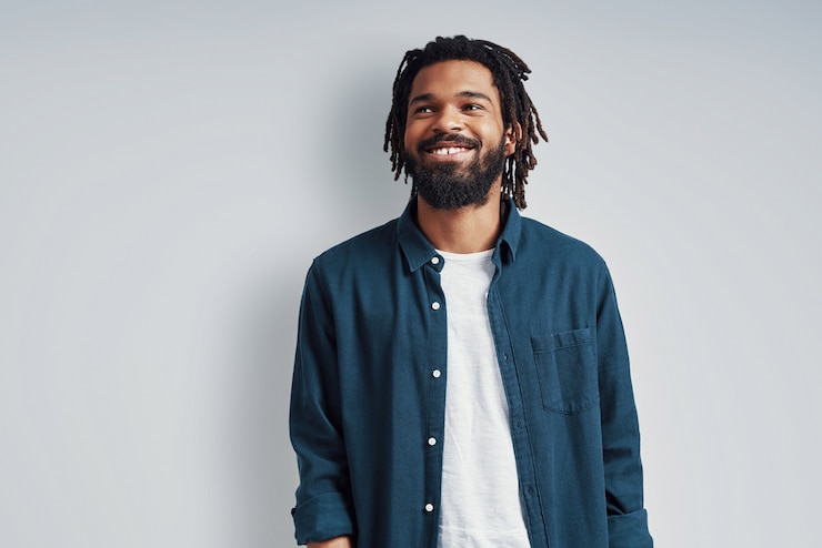 Photo charming young man in casual wear smiling and looking away while standing against grey wall