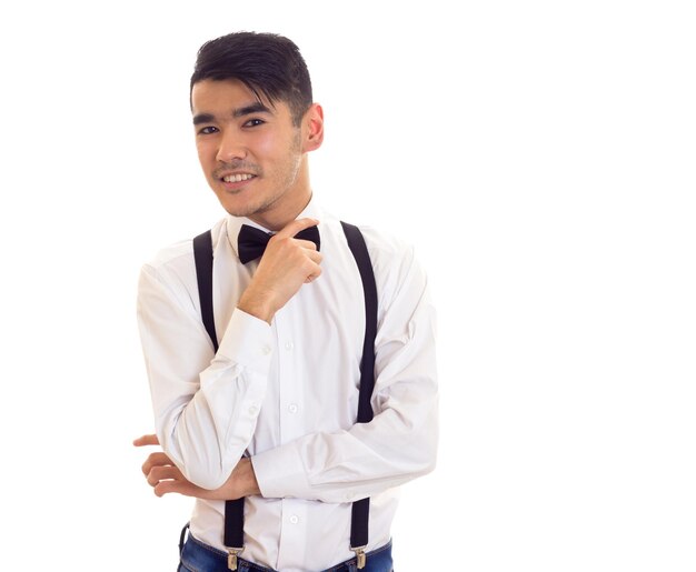 Charming young man in white shirt with black bowtie and suspenders on white background in studio