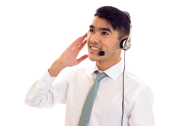 Charming young man with dark hair in white shirt with blue tie using headphones in studio