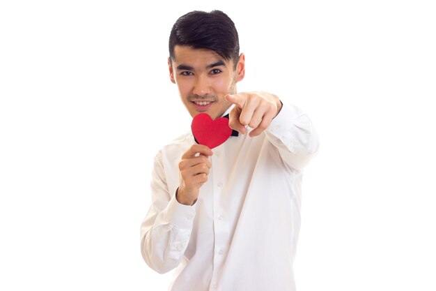 Charming young man with dark hair in white Tshirt with black bowtie holding a red paper heart