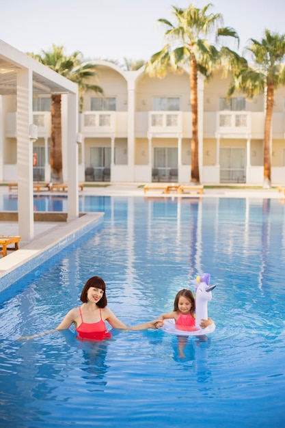 Charming young mom in a pink swimsuit holding hand of her beautiful little daughter in a lifebuoy