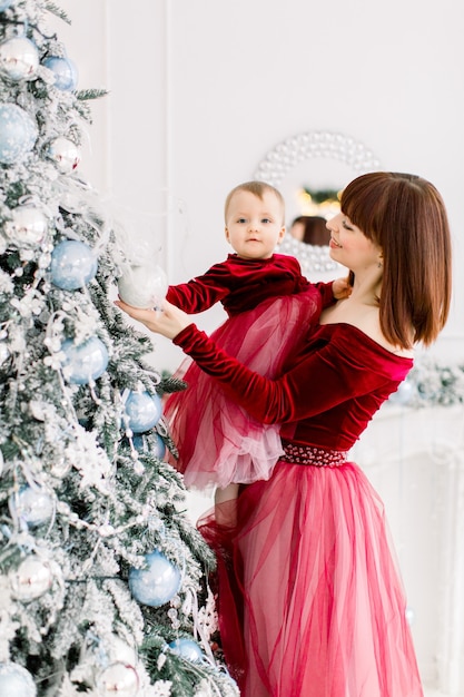 그녀의 귀여운 작은 딸을 잡고 크리스마스 트리를 장식하는 매력적인 젊은 어머니