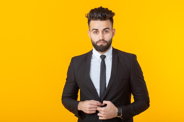 Charming young self-confident businessman wearing formal clothes posing on a yellow wall