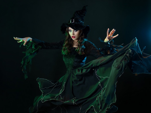 A charming young witch in a costume makes magical passes with two hands