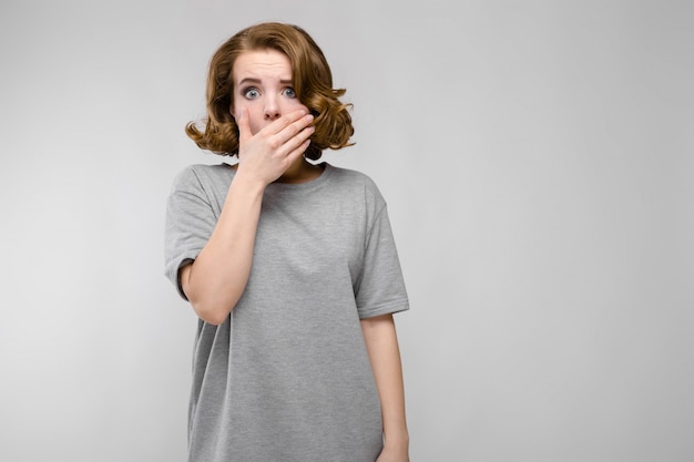 Charming young woman in a gray T-shirt. The woman covered her mouth with her hand