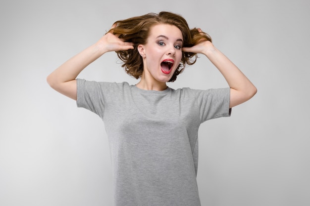 Charming young woman in a gray T-shirt. The woman holds her hands behind her head and screams