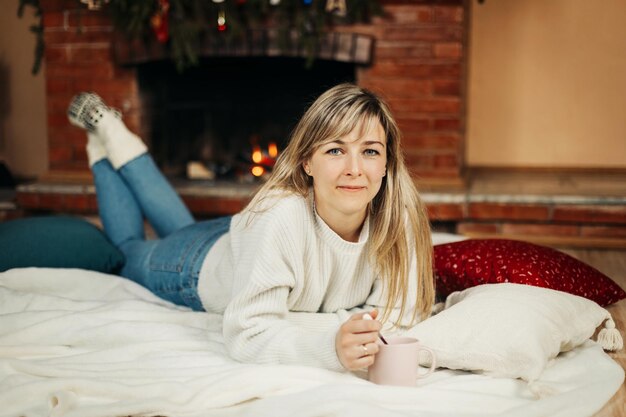 Photo a charming young woman lies on a rug by the fireplace on christmas eve