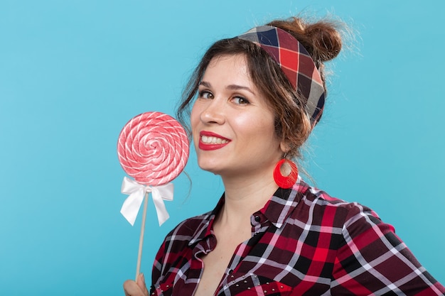 Photo charming young woman in retro clothes holding colorful lollipops in her hands and licking one posing