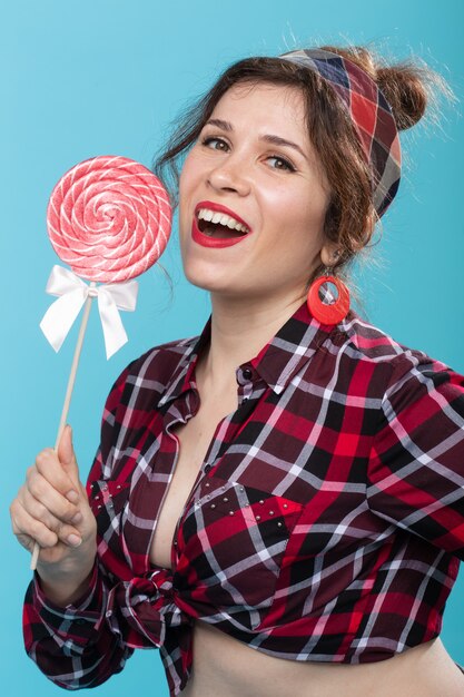 Charming young woman in retro clothes holding colorful lollipops in her hands and licking one posing