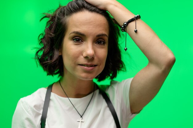 La giovane donna affascinante raddrizza i suoi capelli che posano su un fondo verde. ritratto femminile su chroma key.