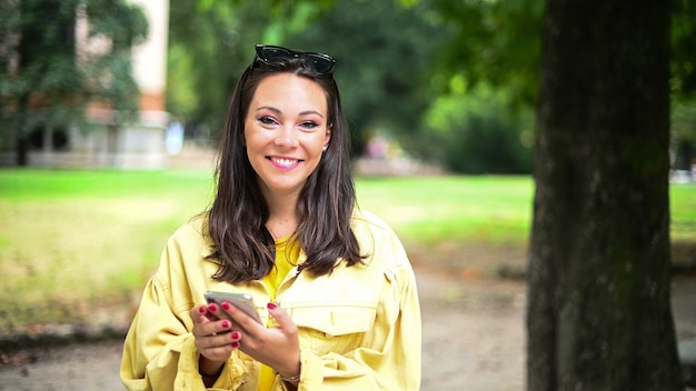 Charming young woman using her smartphone in the park and laughing