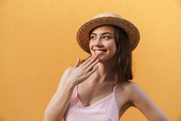 charming young woman wearing summer straw hat smiling and looking aside isolated on yellow