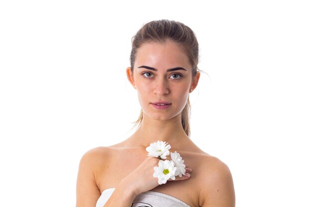 Charming young woman with long brown ponytail holding white flowers on white background in studio